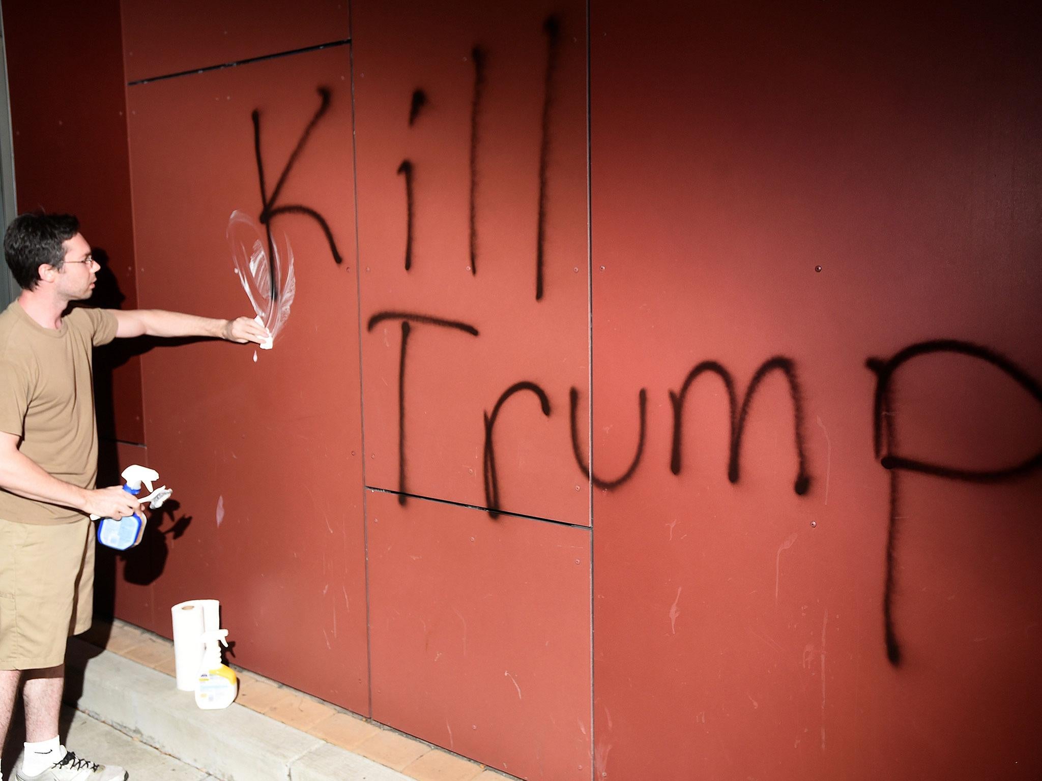 &#13;
A man tries to remove 'Kill Trump' graffiti in Oakland, California (Noah Berger/Reuters)&#13;