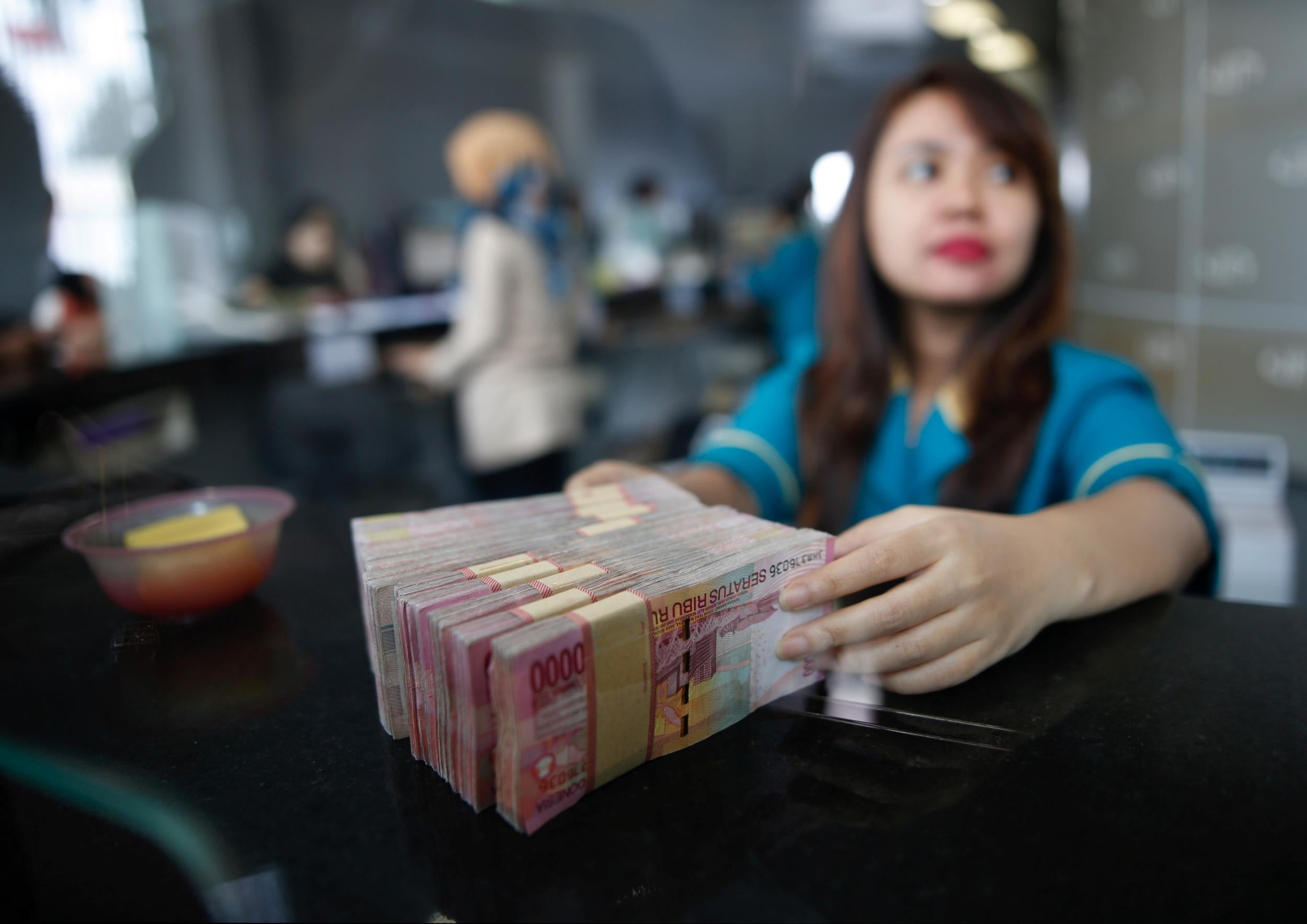 A teller at a money changer handles Indonesia rupiah bank notes in Jakarta