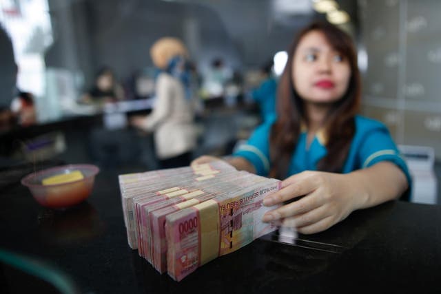 A teller at a money changer handles Indonesia rupiah bank notes in Jakarta