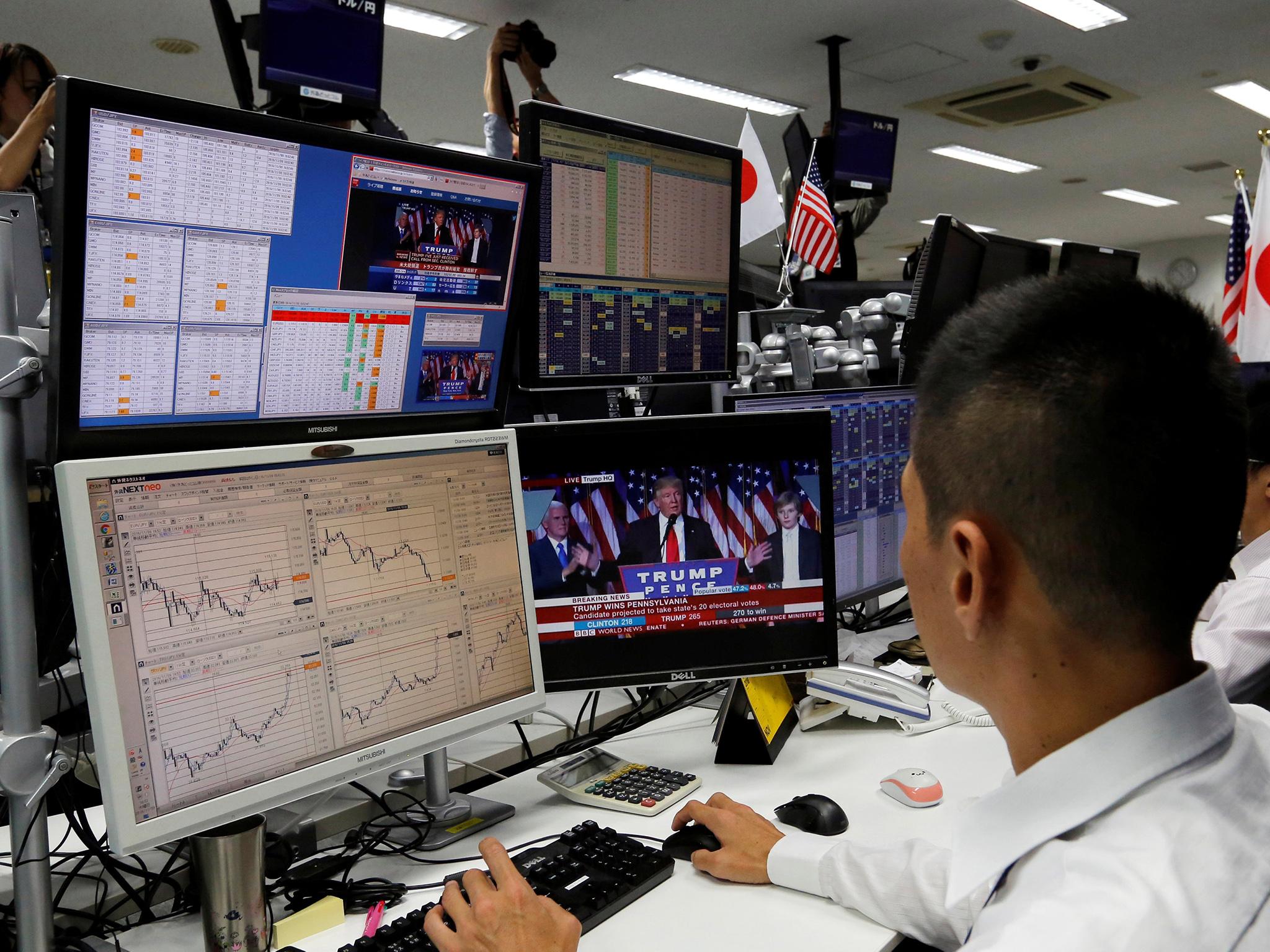 An employee of a foreign exchange trading company looks at monitors showing US President-elect Donald Trump speaking on TV news in Tokyo, Japan