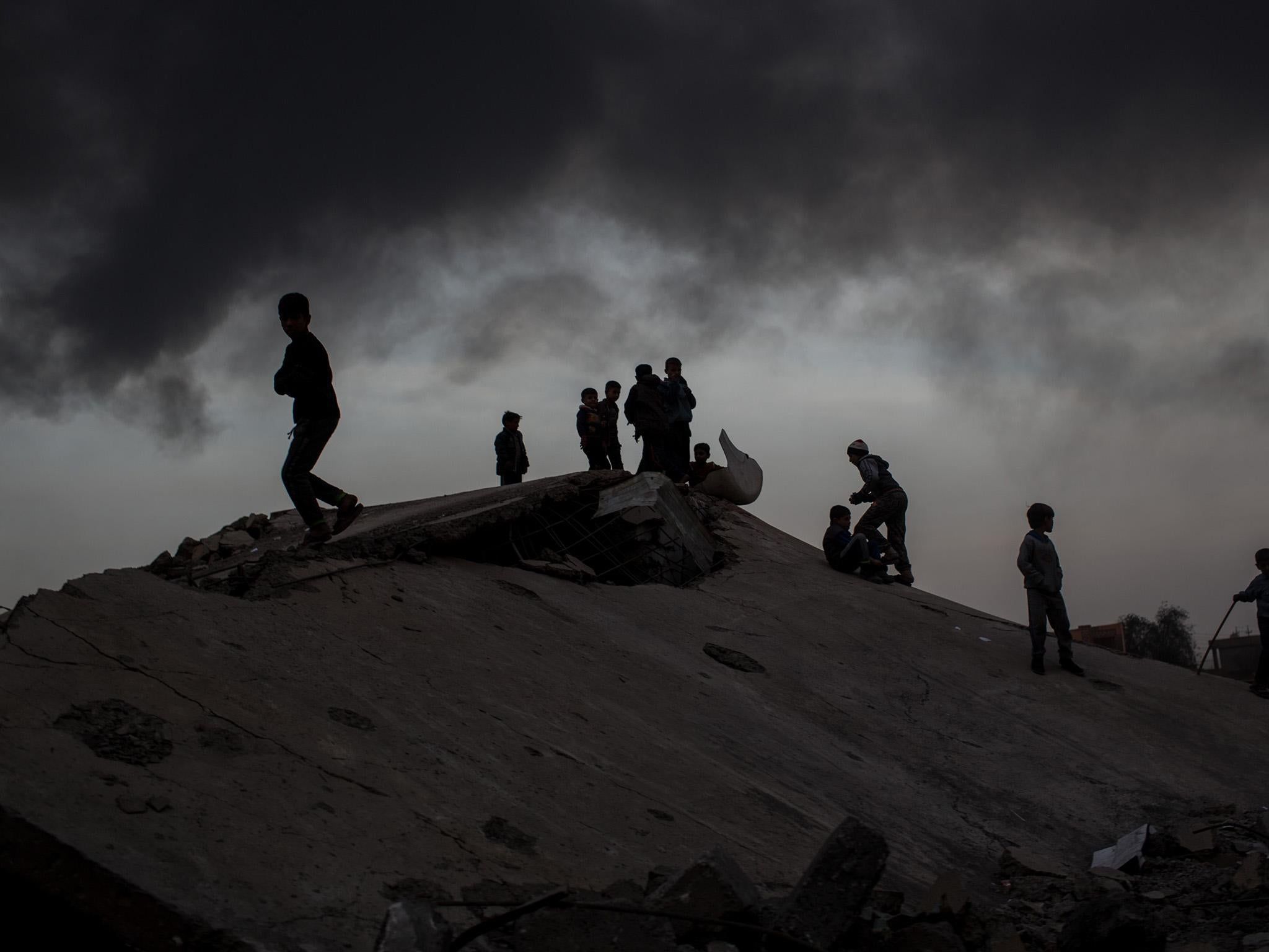 Children play on rubble at a destroyed football stadium