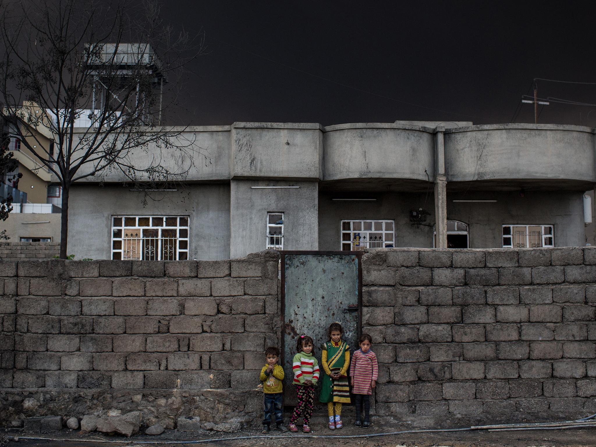 Children standing outside their home in a street close to a burning oil well