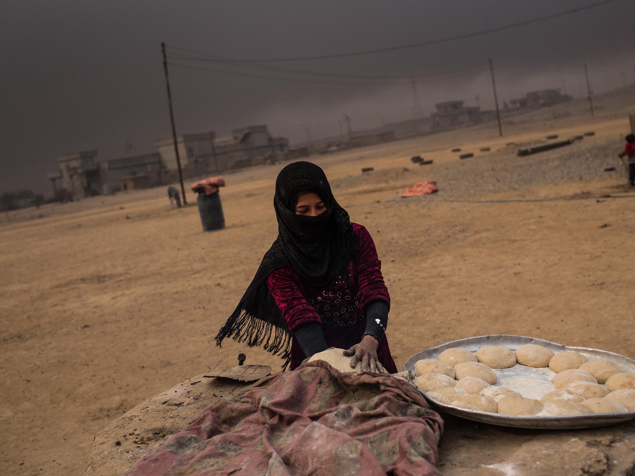 A woman makes bread under smoke-filled skies