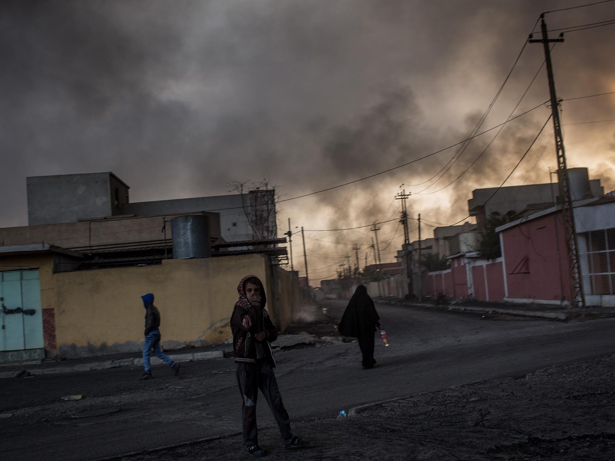 A young boy covers his mouth as heavy smoke from burning oil wells fills the sky