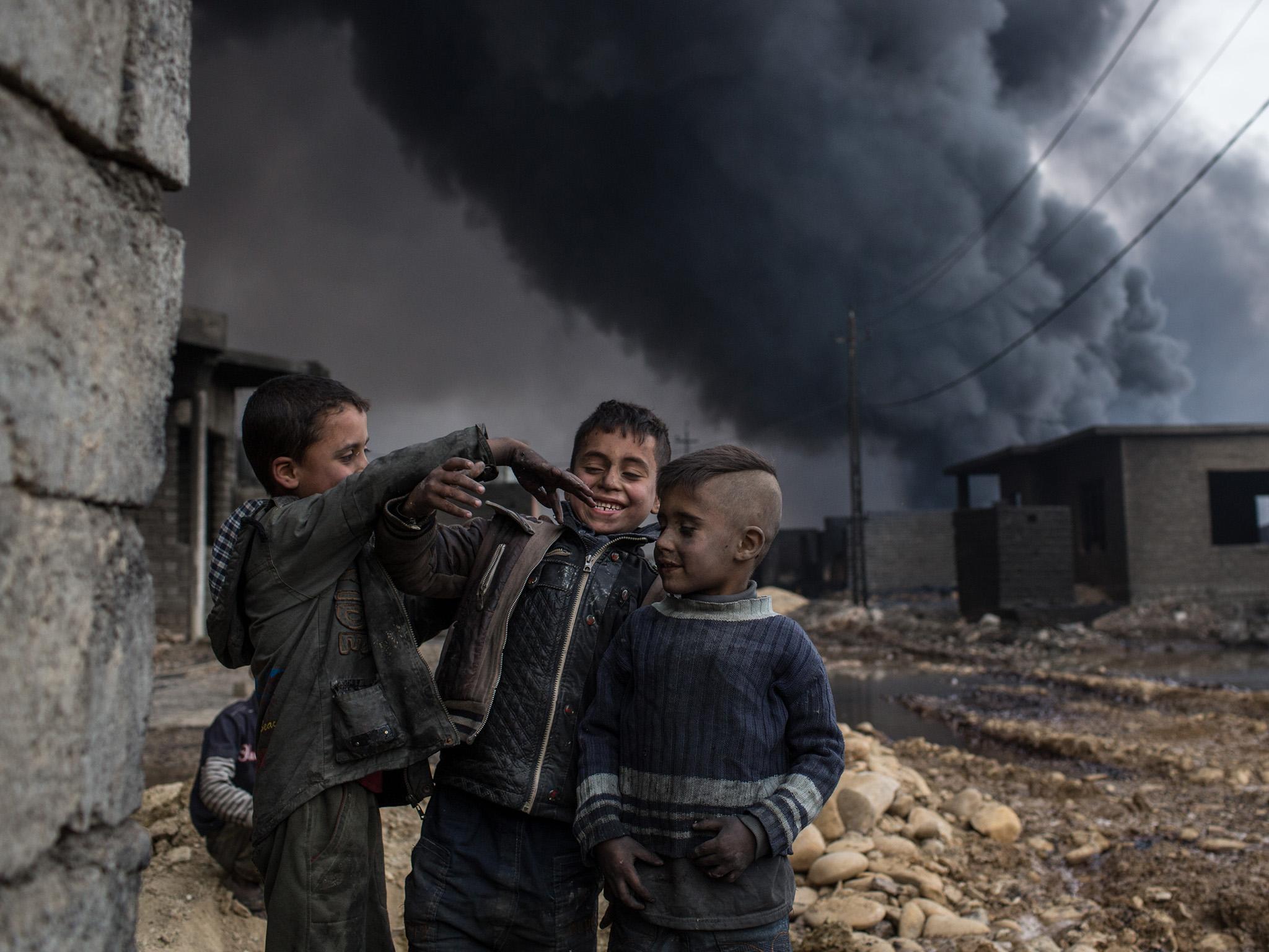 Boys play in a street outside their home in front of a burning oil well set on fire by fleeing Isis members