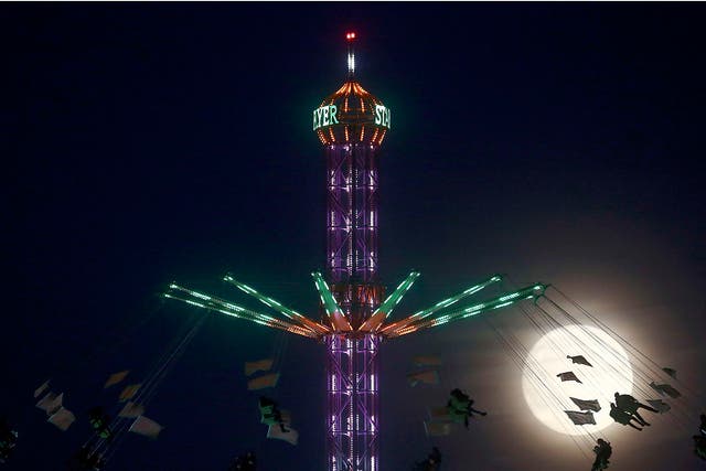 People on a funfair ride are silhouetted against the moon in London