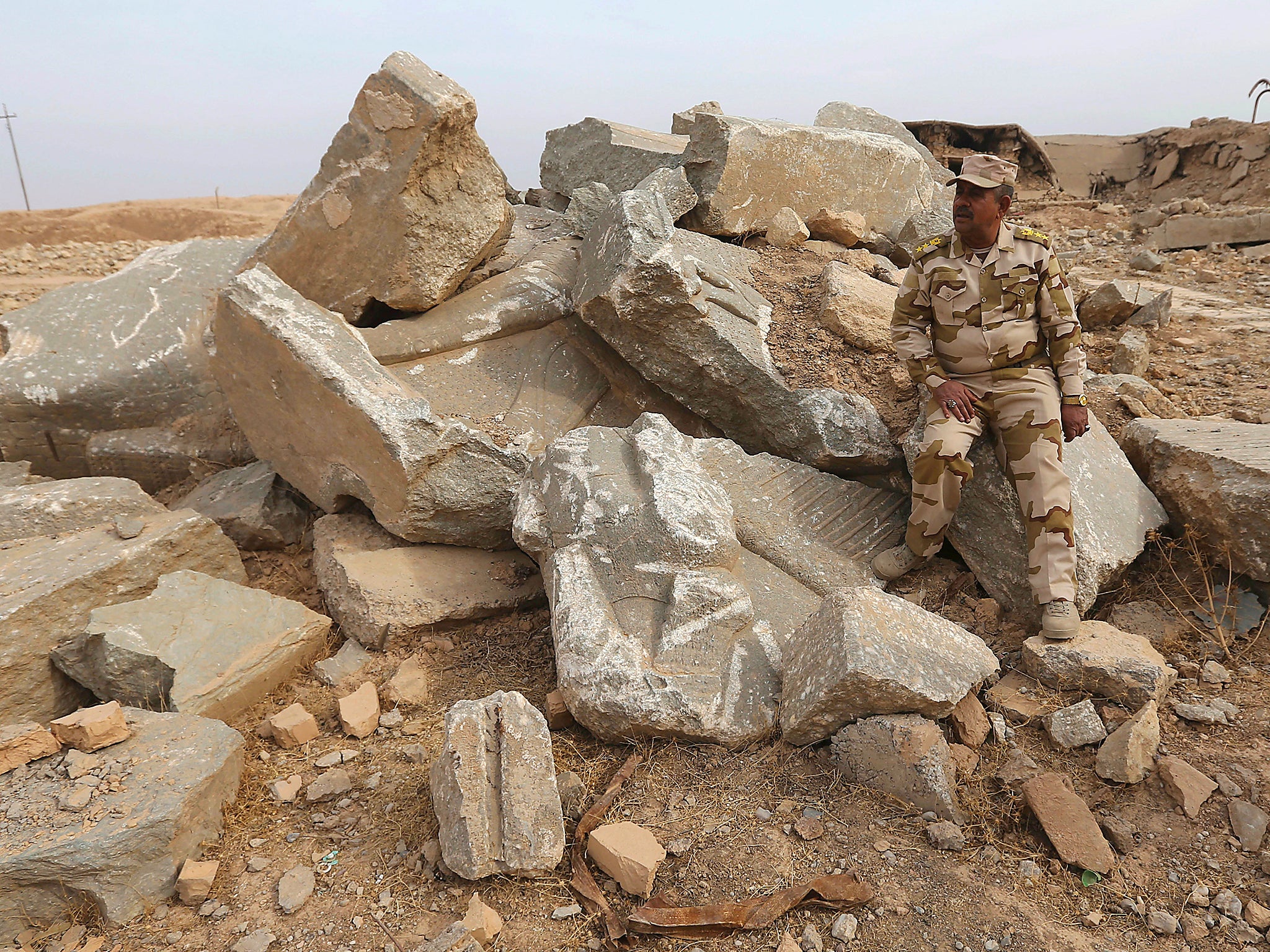 An Iraqi army officer sits on damaged carved stone slabs, which were destroyed by Islamic State militants, at the ancient site of Nimrud