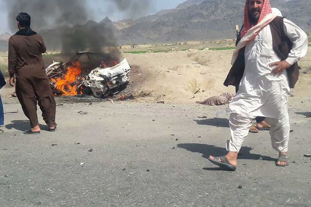 Pakistani local residents gathering around a destroyed vehicle hit by a drone strike in which Afghan Taliban Chief Mullah Akhtar Mansour was believed to be travelling