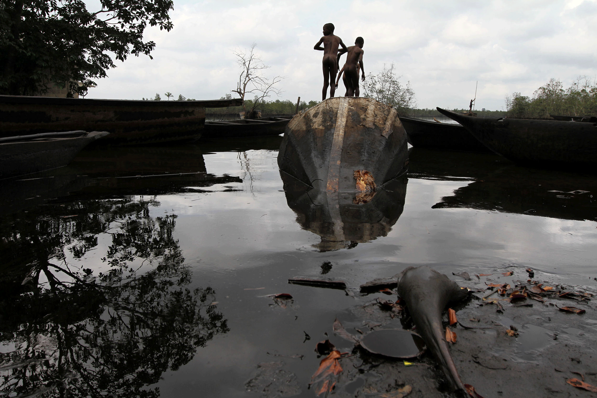 Children play on an abandoned canoe at the bank of a polluted river in Bidere community in Ogoniland