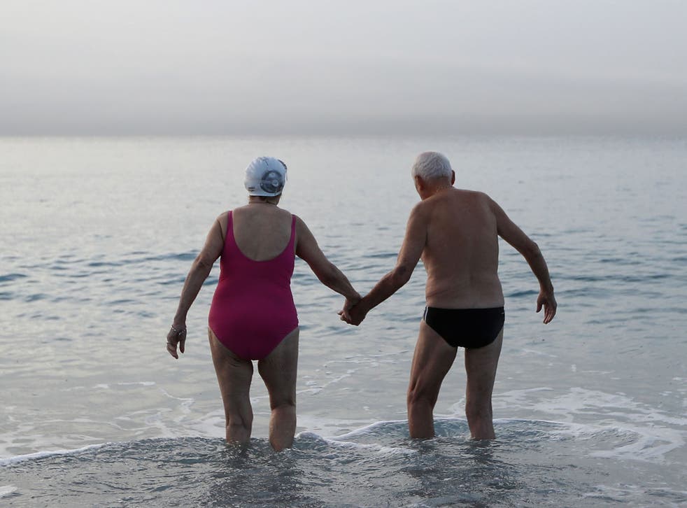 An elderly man and woman hold hands as they walk into the Mediterraneean Sea in the French riviera city of Nice