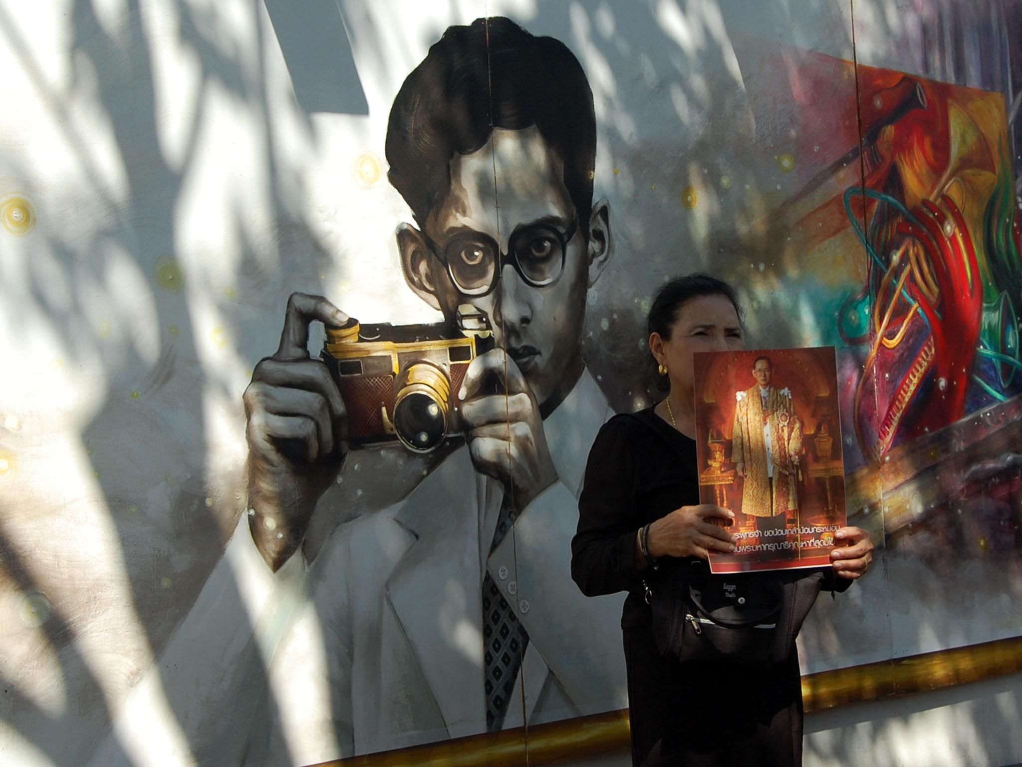 Mourners hold posters of the late king as they walk, taking photos beside a mural depicting his work and passion for the arts