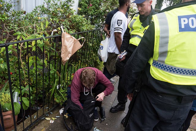 Police officers inspect the content of a man's rucksack containing canisters of nitrous oxide
