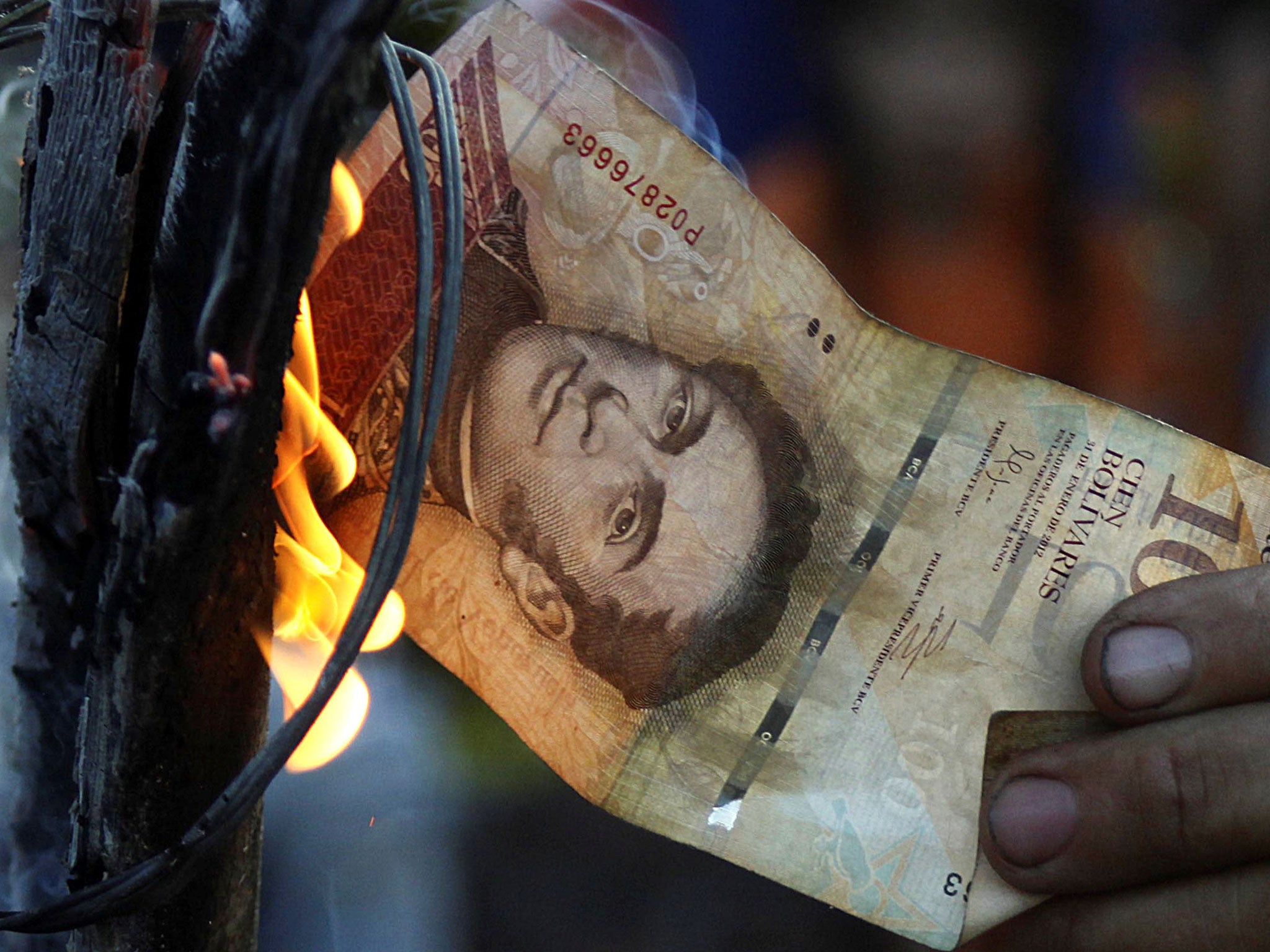 A man burns a 100-bolivar bill during a protest in El Pinal