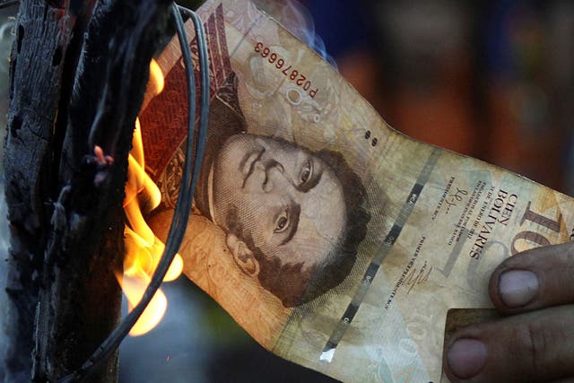 A man burns a 100-bolivar bill during a protest in El Pinal