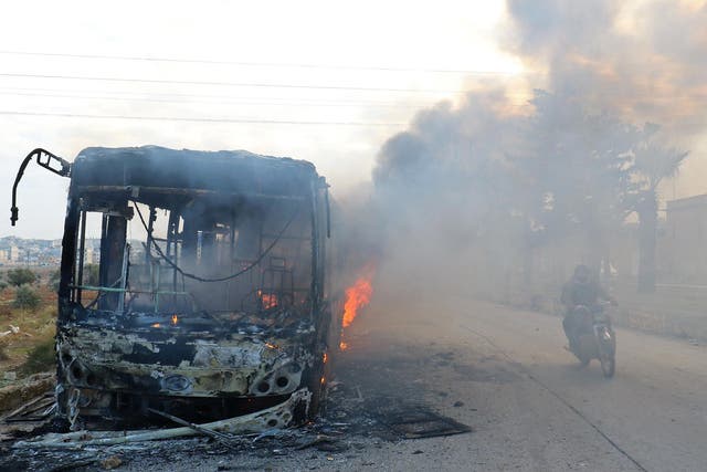 A man on a motorcycle drives past burning buses while en route to evacuate ill and injured people from the besieged Syrian villages of al-Foua and Kefraya, after they were attacked and burned, in Idlib province, Syria