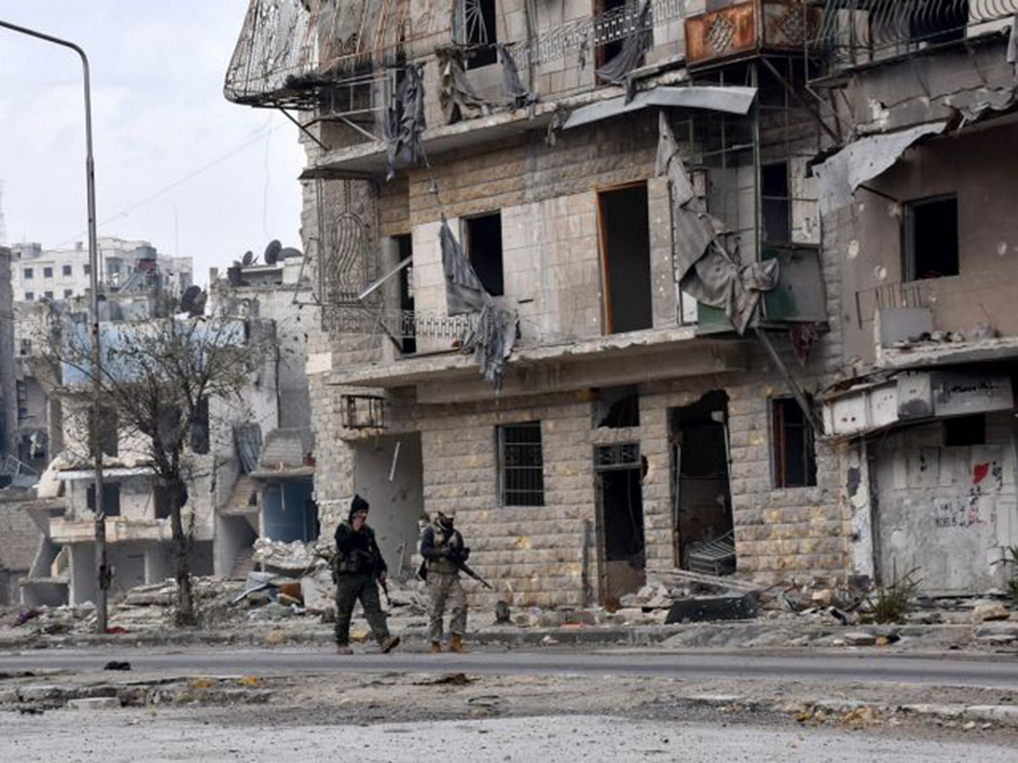 Armed men walk through the ruined Al-Sukari and Ansari district in Aleppo on Thursday