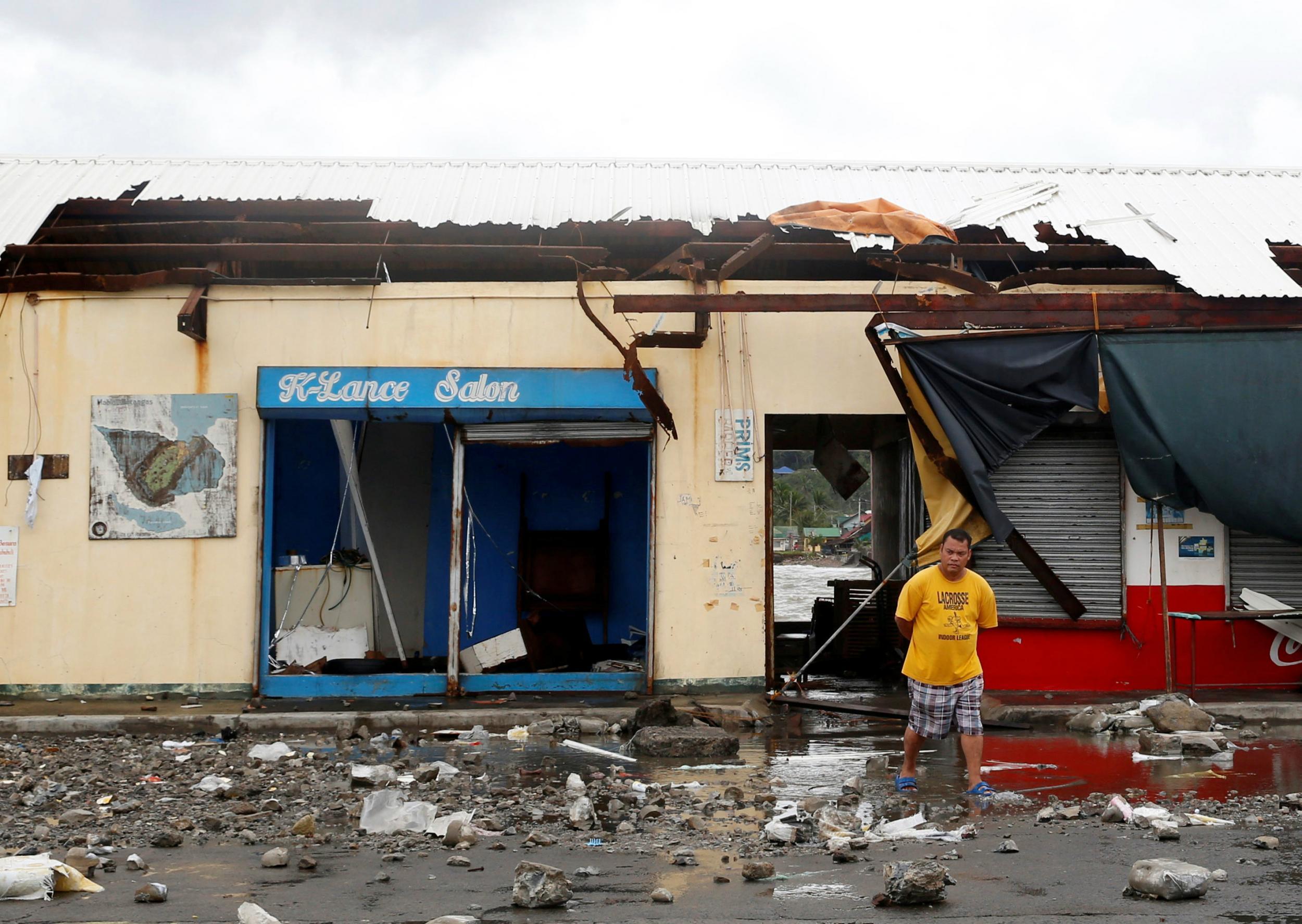 A resident walks in front of a partially damaged port building and debris swept from the sea at the height of Typhoon Nock-Ten in Mabini, Batangas, in the Philippines