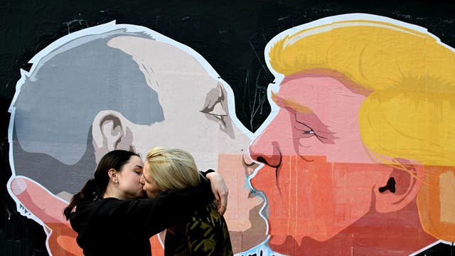 A lesbian couple kisses in front of mural depicting Russian President Vladimir Putin and Republican presidential candidate Donald Trump, on the walls of a barbecue bar 'Keule Ruke' on May 19, 2016 in Vilnius, Lithuania.