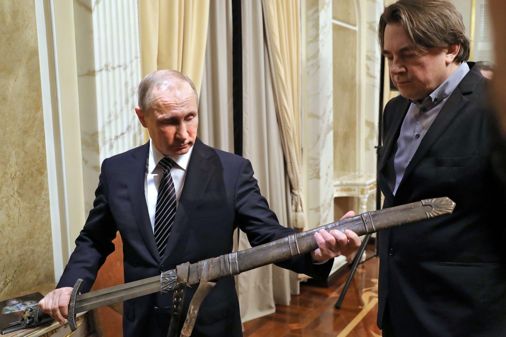 Russian President Vladimir Putin (L) holds a cinema replica of a sword as he speaks with film producer and Channel One CEO Konstantin Ernst during a meeting with the crew of The Viking film based on the Primary Chronicle, on December 30, 2016 in Moscow