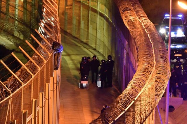Spanish border guards look on as a migrant attempts to climb the fences in ceuta