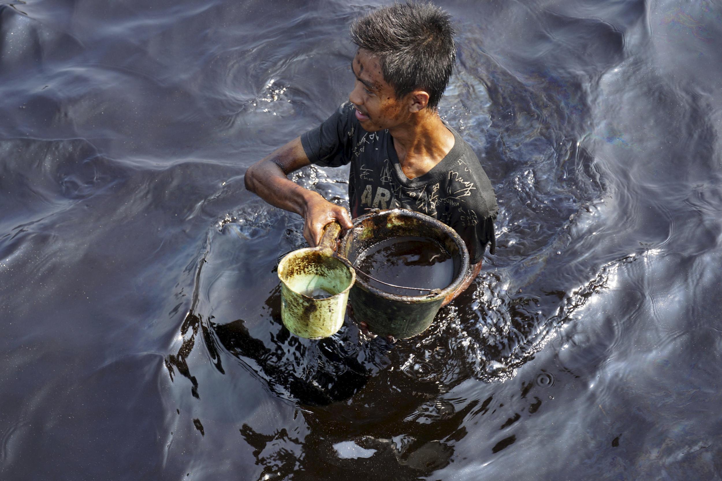 A fisherman collects spilled crude oil at the Pantai Teluk Penyu in Cilacap, Indonesia