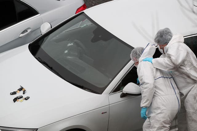 Police forensics officers examine a silver Audi with bullet holes in its windscreen at the scene near junction J24 of the M62 in Huddersfield