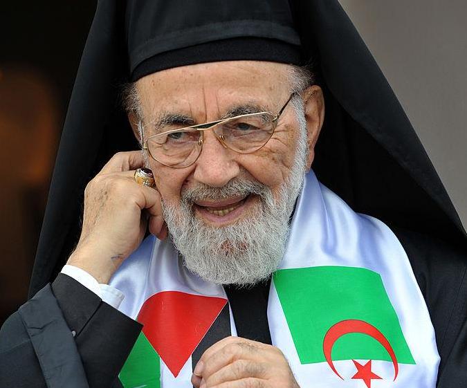 Archbishop Hilarion Capucci, with both Algerian (R) and Palestinian (L) flags on his outfit, smiles during an international Arab conference in support of Palestinian prisoners in Israeli jails on December 5, 2010 in Algiers