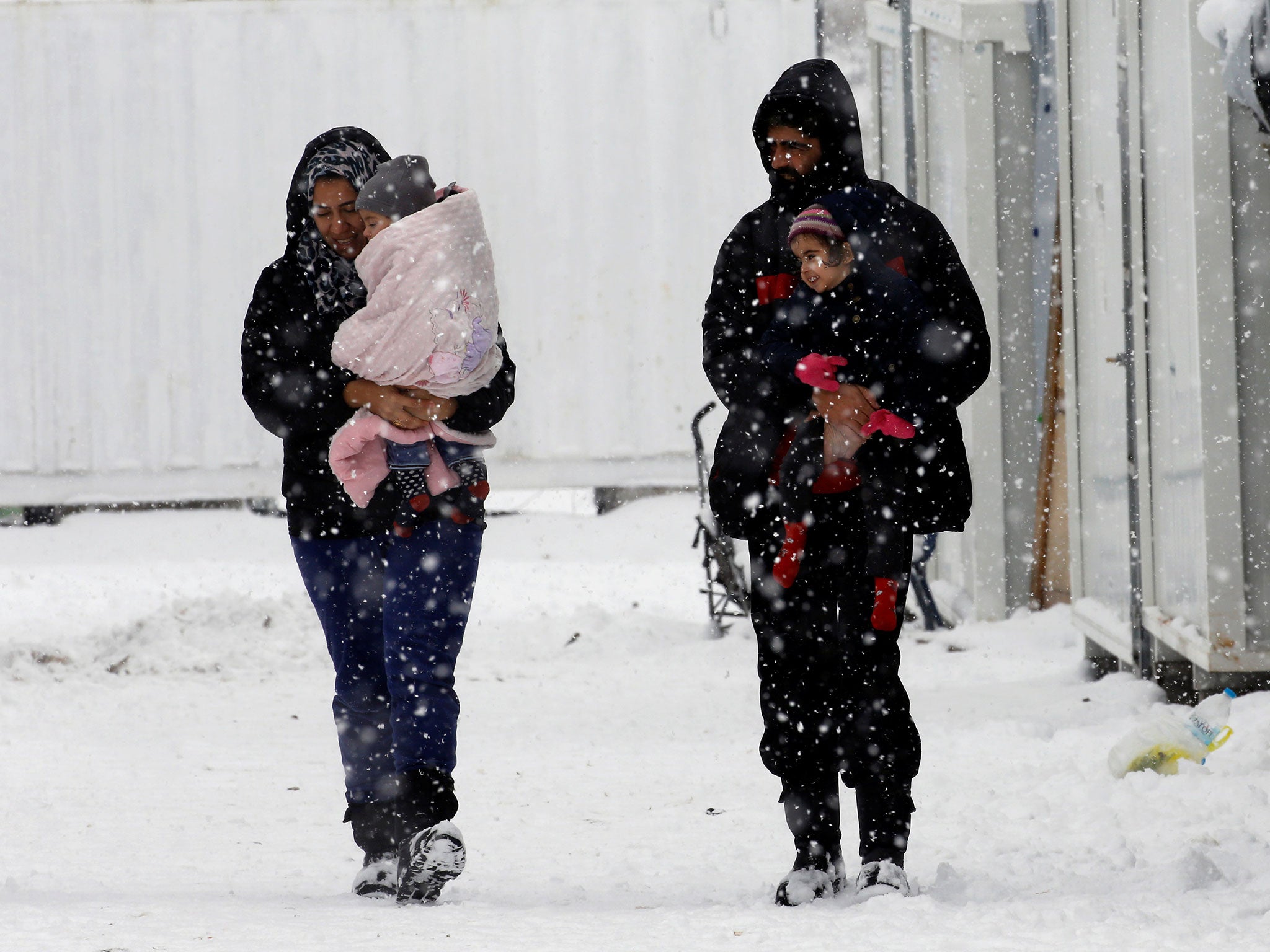 Syrian refugees carry their children through a snow storm at a refugee camp north of Athens, Greece, on 10 January