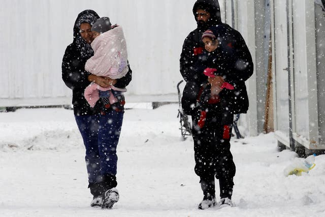 Syrian refugees carry their children through a snow storm at a refugee camp north of Athens, Greece, on 10 January