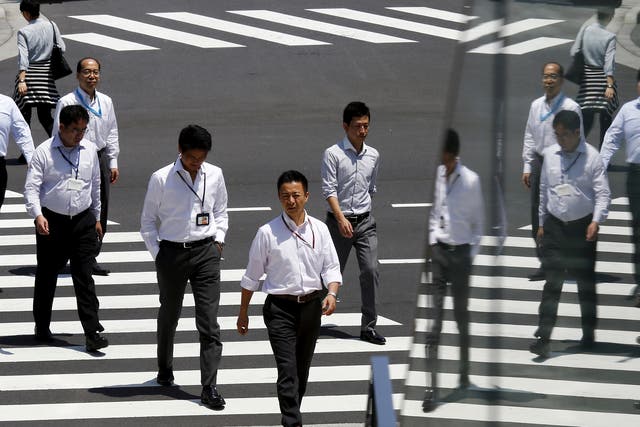 Office workers are reflected in a glass railing as they cross street during lunch hour in Tokyo