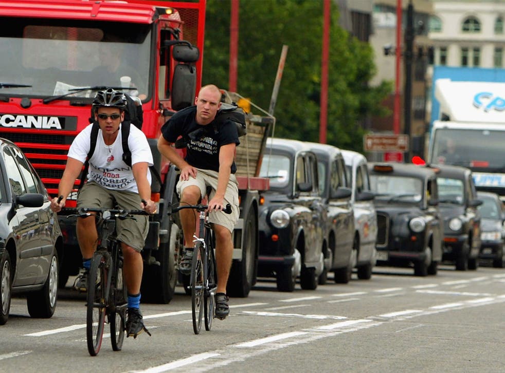 Cyclists pass a line of stationary traffic in London
