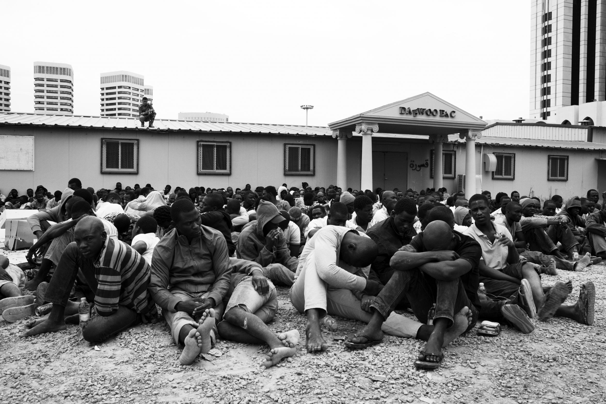 A group of migrants detained under armed guard by militia men at an abandoned industrial park in Tripoli, Libya