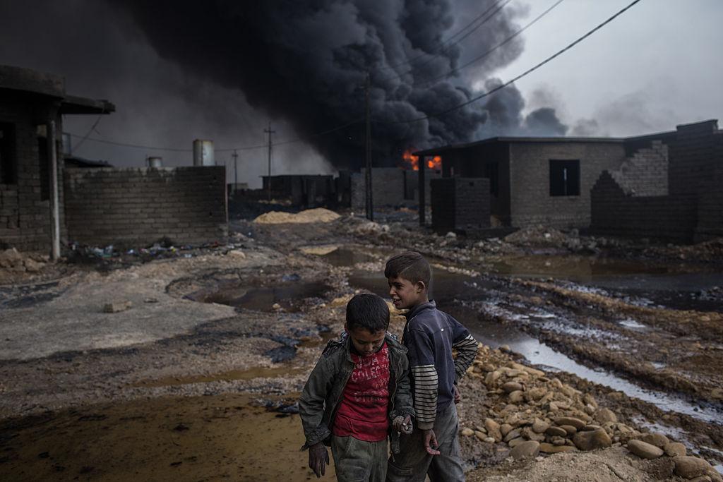 Two boys play outside their home in front of a burning oil well set on fire by fleeing Isis members on November 10, 2016 in Al Qayyarah, Iraq