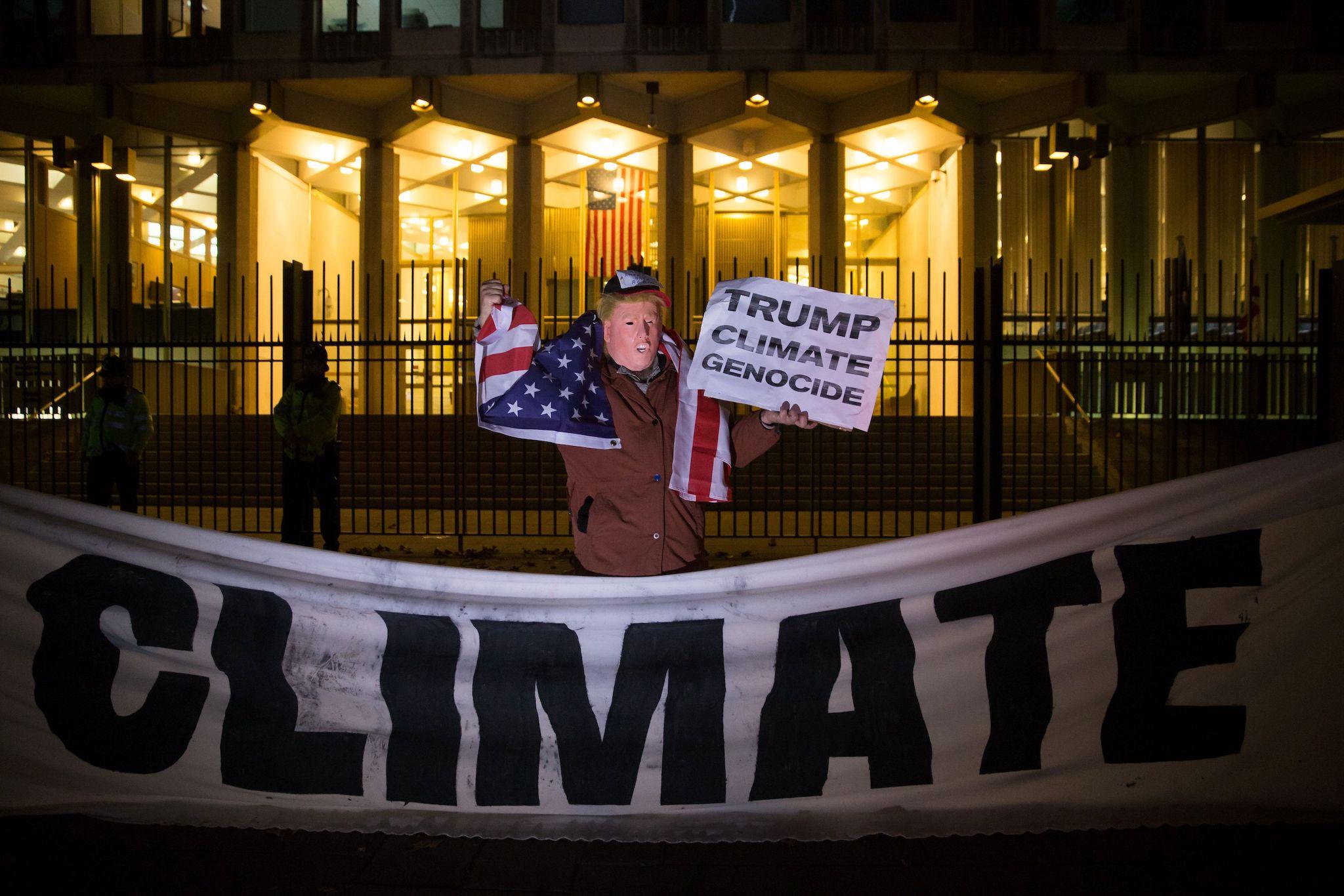 A man wearing a mask portraying newly elected US president-elect Donald Trump poses with a sign during a demonstration against Trump's vow to withdraw the US from the Paris Climate Accord outside the US Embassy in central London in November 18, 2016