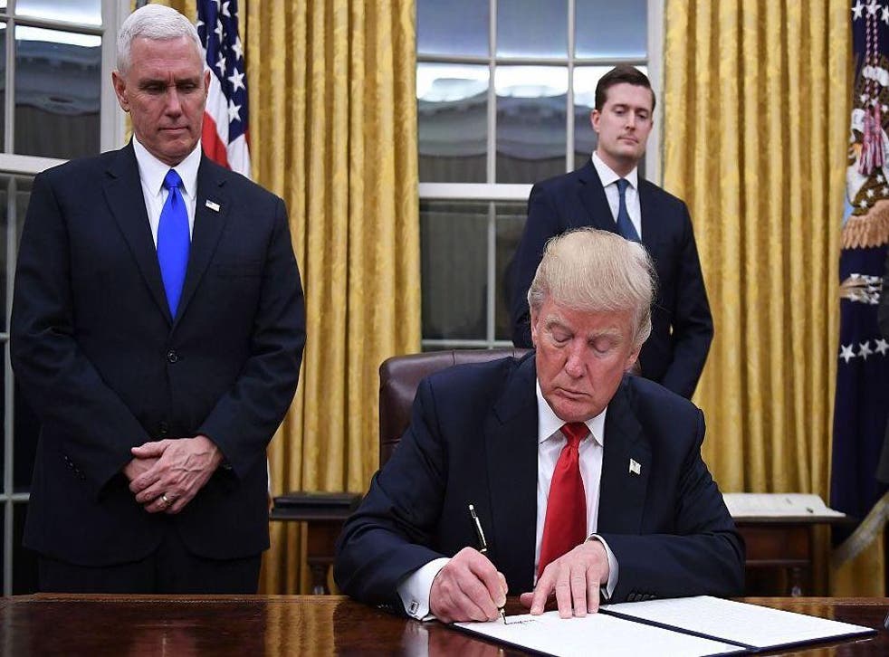 President Donald Trump signs an executive order as Vice President Mike Pence looks on at the White House in Washington, DC on January 20, 2017.