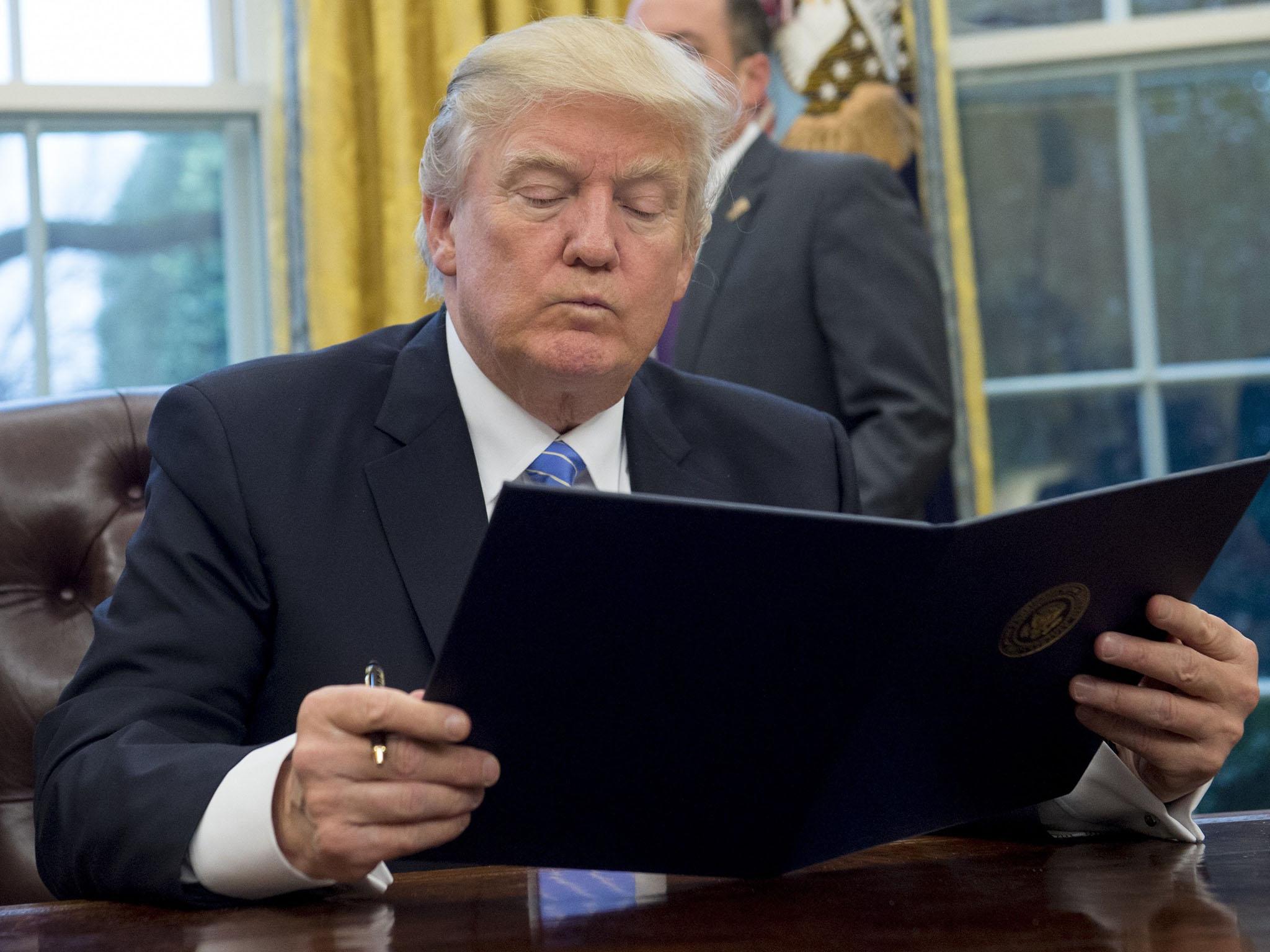 US President Donald Trump reads an executive order withdrawing the US from the Trans-Pacific Partnership prior to signing it in the Oval Office of the White House in Washington, DC, January 23, 2017