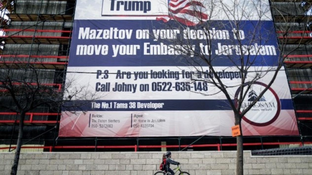 A child cycles past a giant banner bearing a message of congratulations ("Mazeltov") for incoming US President Donald Trump, covering a building under construction in central Jerusalem on January 20, 2017