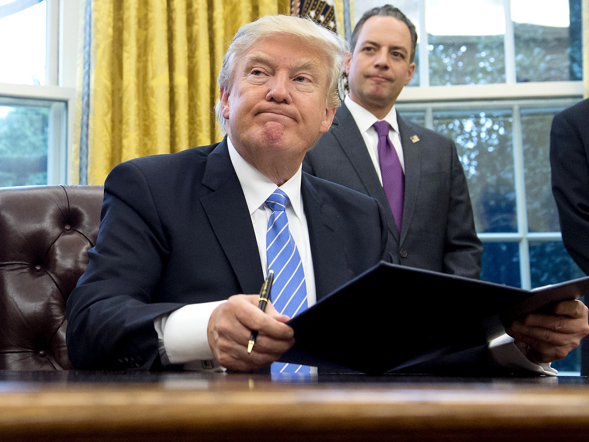 US President Donald Trump signs an executive order as Chief of Staff Reince Priebus looks on in the Oval Office of the White House