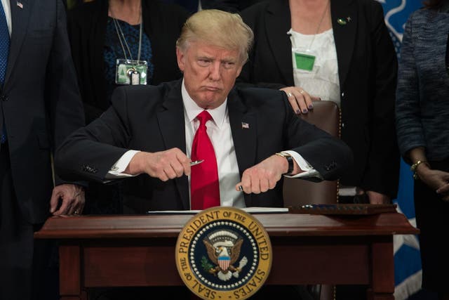 Donald Trump takes the cap off a pen to sign an executive order