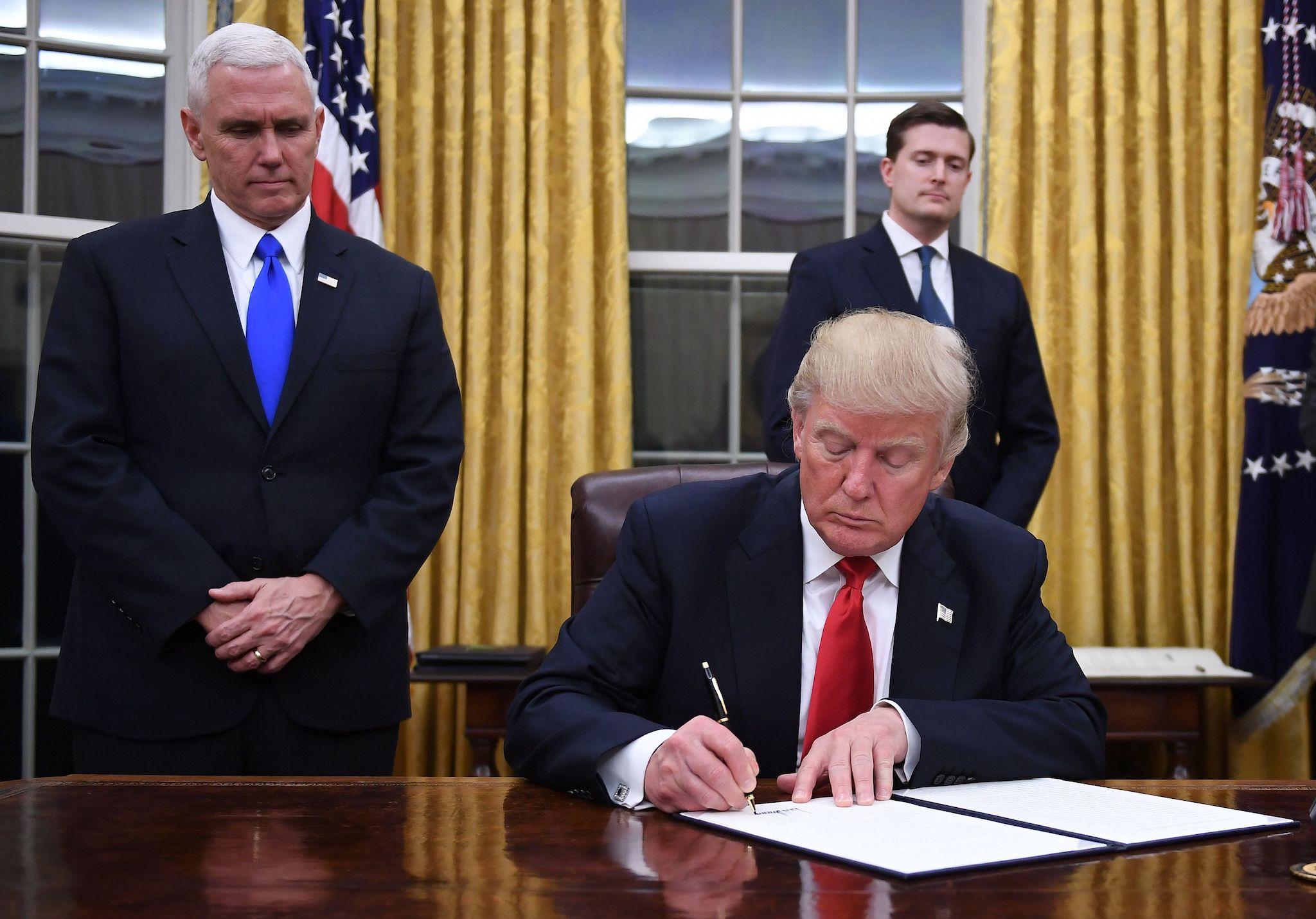 US President Donald Trump signs an executive order as Vice President Mike Pence looks on at the White House in Washington, DC on January 20, 2017