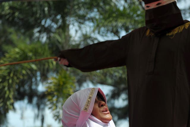 A religious officer canes an Acehnese woman for spending time in close proximity with a man who is not her husband, which is against Sharia law, in Banda Aceh