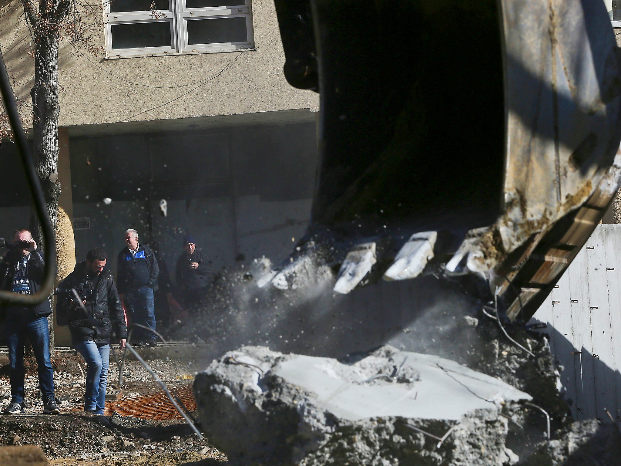 Kosovo Serbs look as bulldozers tear down a concrete wall erected in the northern city of Mitrovica