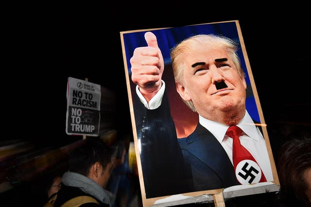 A demonstrator holds a placard showing a picture of US President-elect Donald Trump modified to add a swastika and an Adolf Hitler-style moustache during a protest outside the US Embassy in London