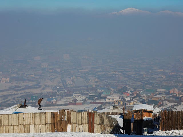 A man walks on the roof of a traditional ger home while fixing the chimney of a coal burning stove on a cold hazy day on the outskirts of Ulan Bator