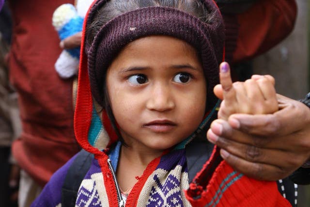 A girl holds up her little finger with purple ink to show she has been given two polio drops