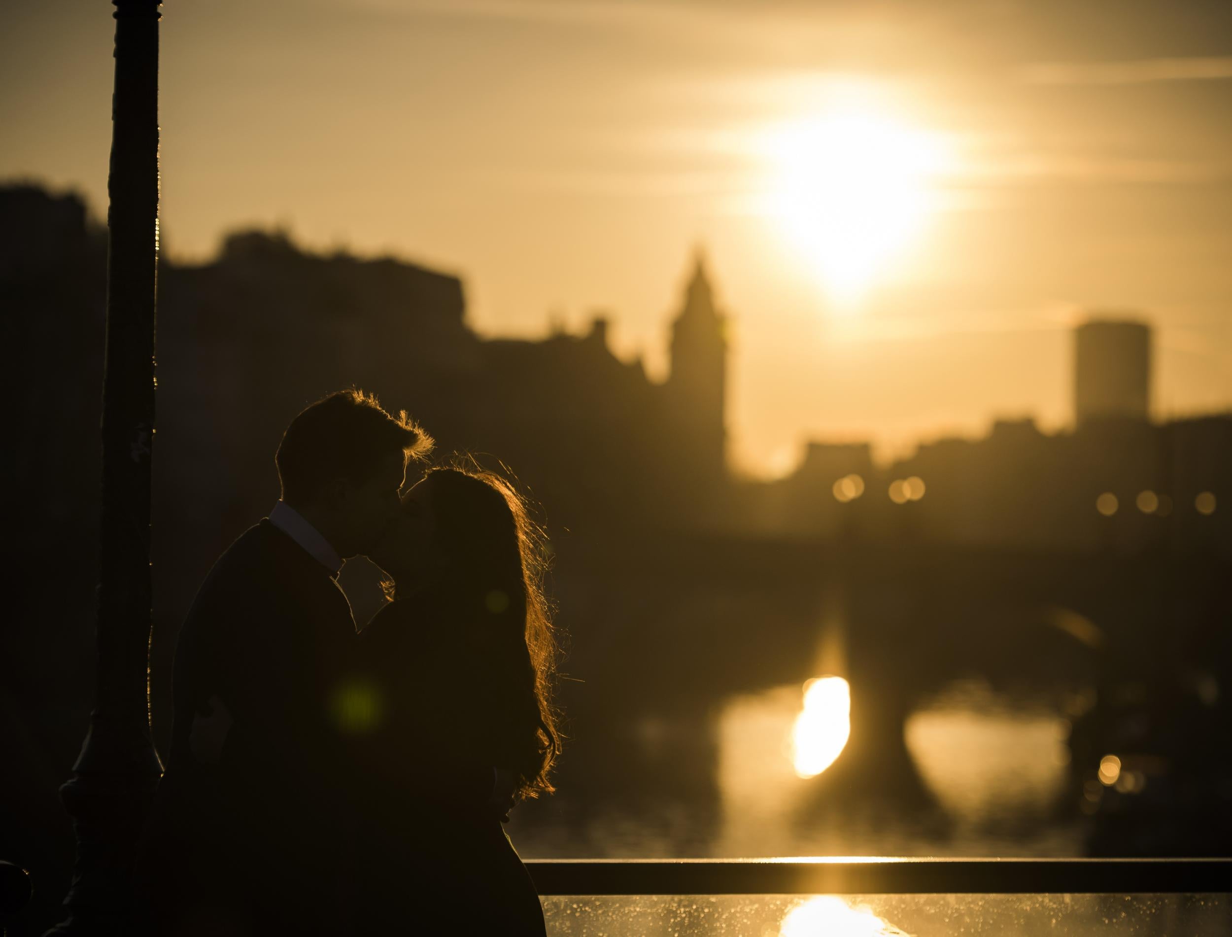 A couple kisses on the Pont des Arts bridge at sunrise