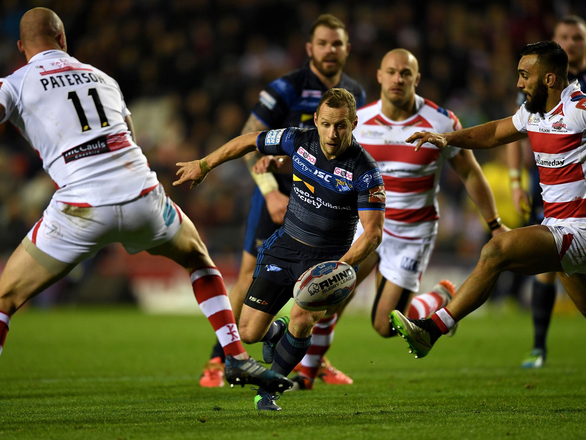 Rob Burrow of Leeds kicks past Cory Paterson of Leigh