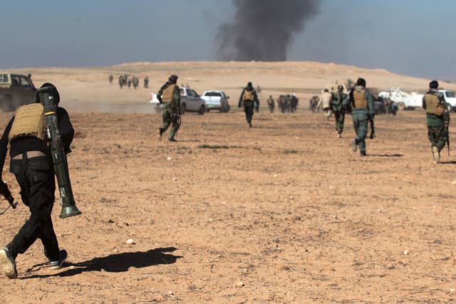 Smoke billows in the background as Iraqi forces, supported by the Hashed al-Shaabi