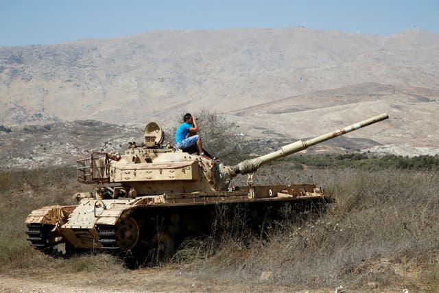 A man sits on an old tank as he watches fighting taking place in Syria as seen from the Israeli side of the border fence between Syria and the Israeli-occupied Golan Heights on September 11, 2
