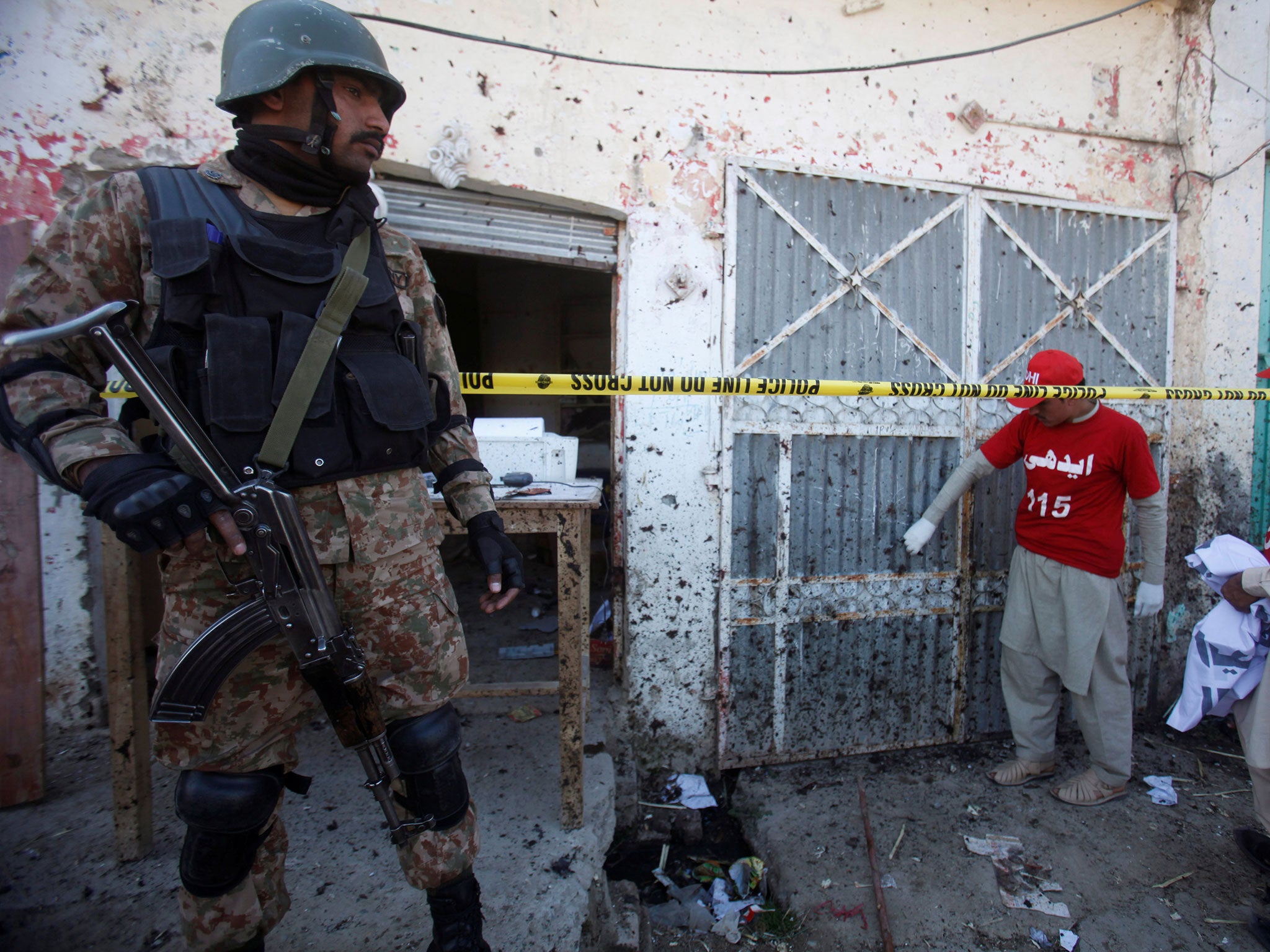 A soldier stands guard as voluteers collect remains of the walls and doors around the site of a blast at the courthouse in Charsadda, Pakistan, 21 February